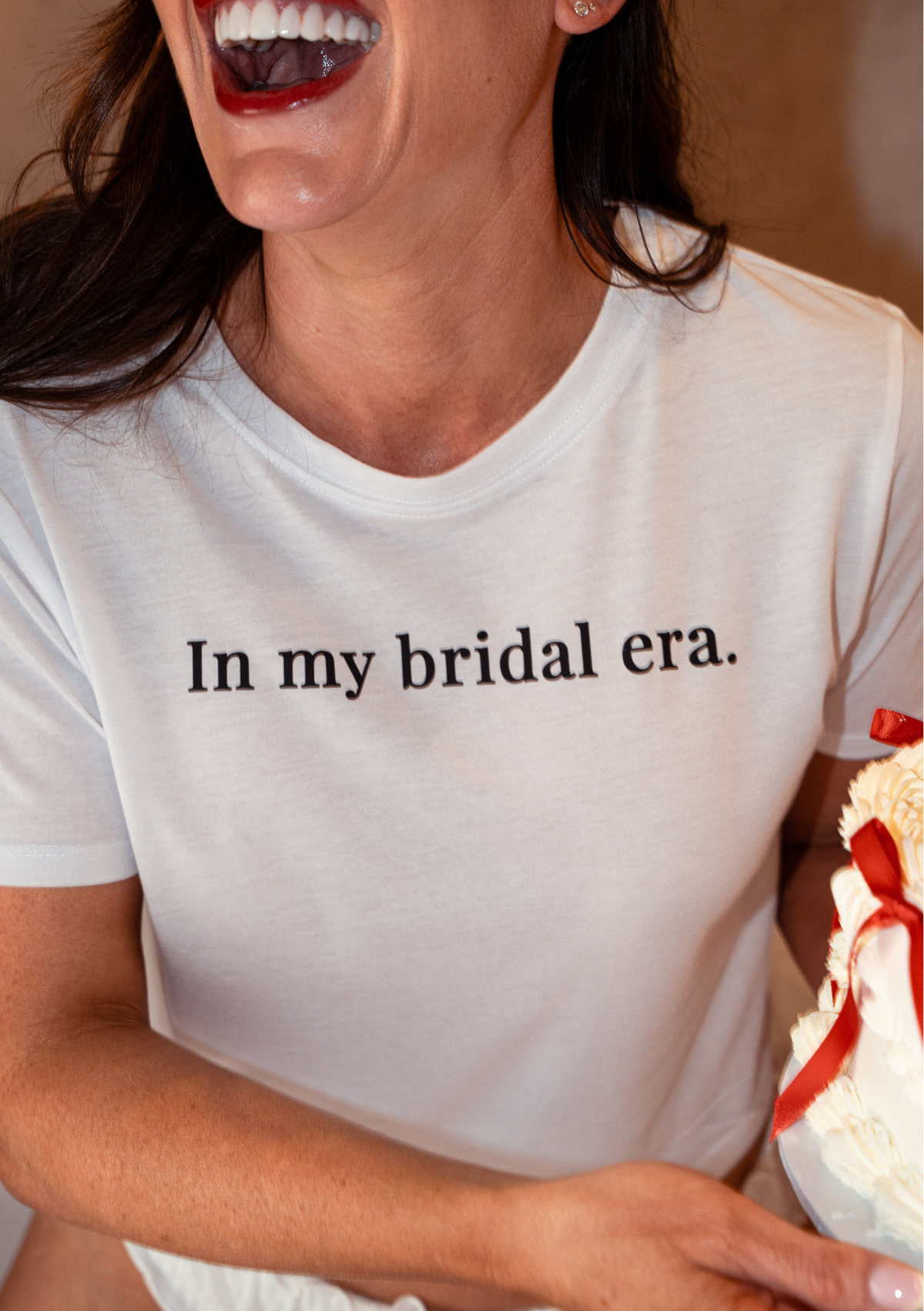 Person wearing a white t-shirt with 'In my bridal era.' text, holding a cake.